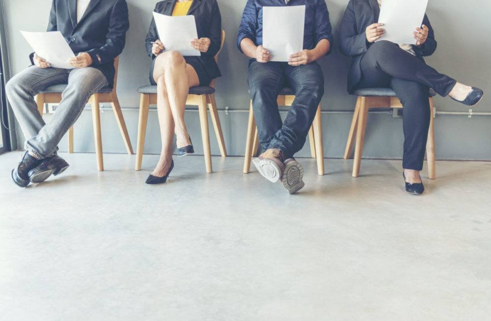 Job candidates sitting in a row holding resumes while waiting for interviews
