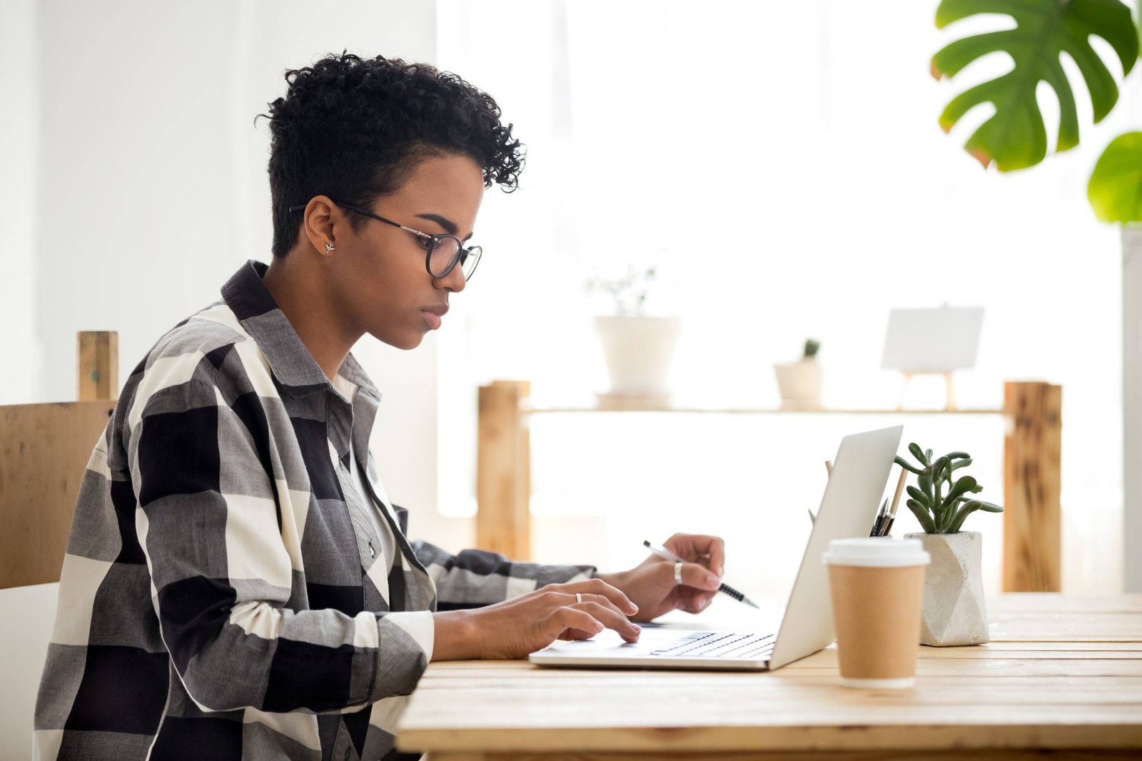 Student in glasses typing on a laptop at a wooden desk