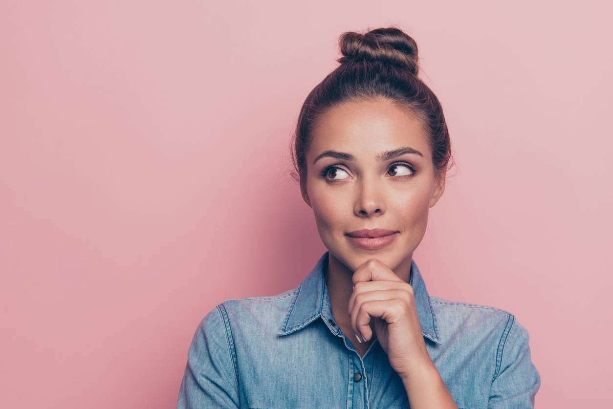Thoughtful woman with her hand on her chin against a pink background