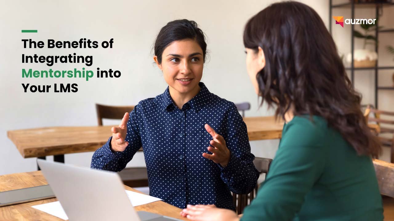 Mentor talking with a colleague at a desk, with the title The Benefits of Integrating Mentorship into Your LMS