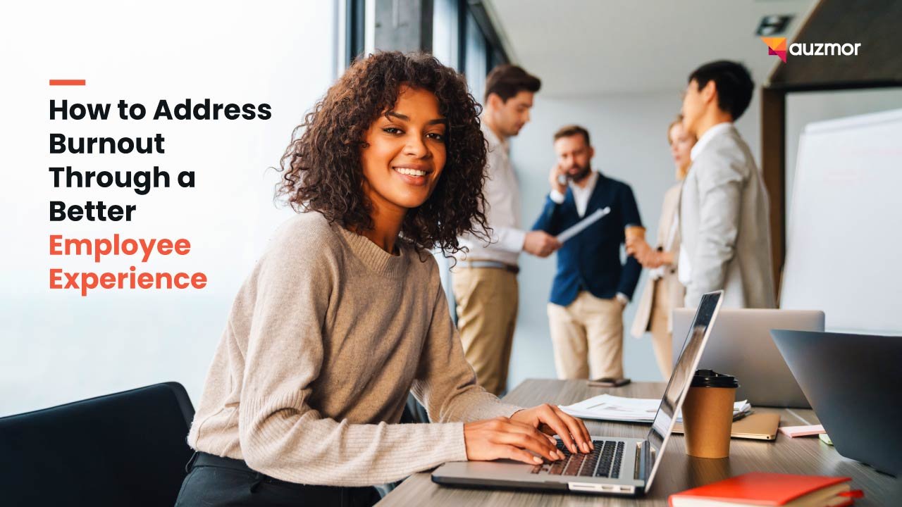 Smiling woman at a laptop with colleagues behind her, with the title How to Address Burnout Through a Better Employee Experience
