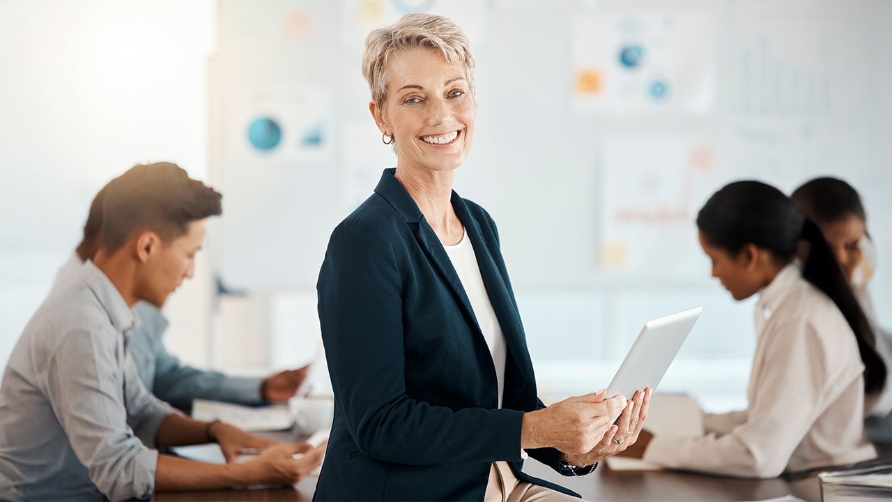 Smiling trainer holding a tablet while colleagues work behind her