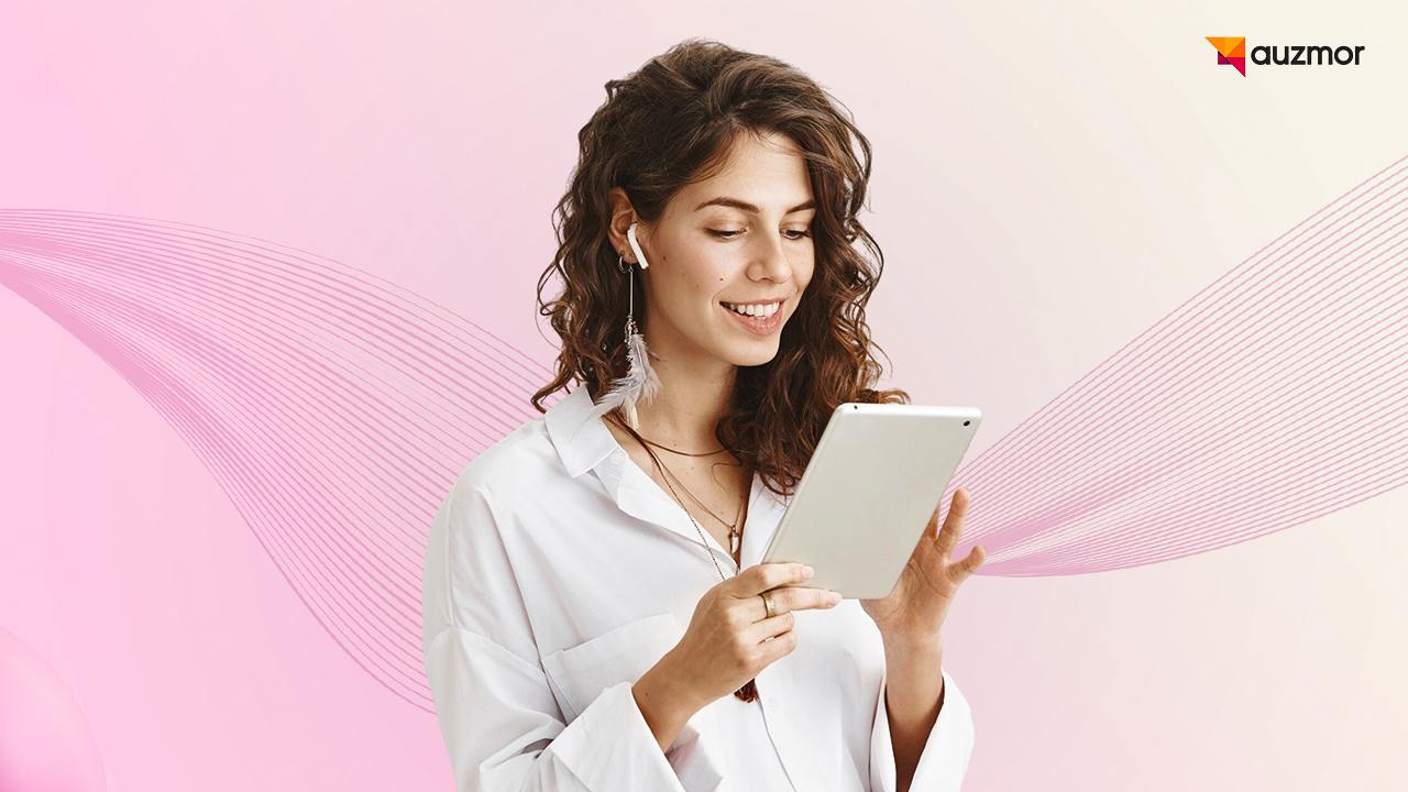 Woman with earbuds smiling at a tablet against a pink background