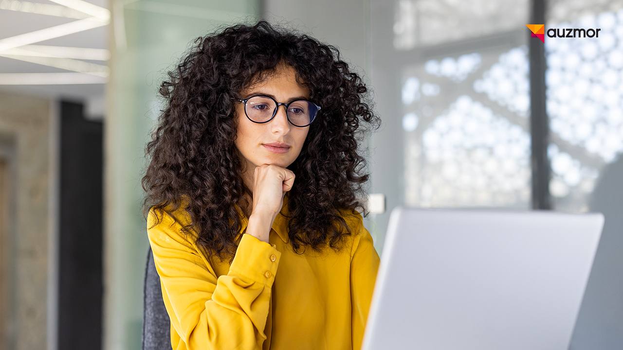 Thoughtful woman in glasses looking at a laptop while planning training content
