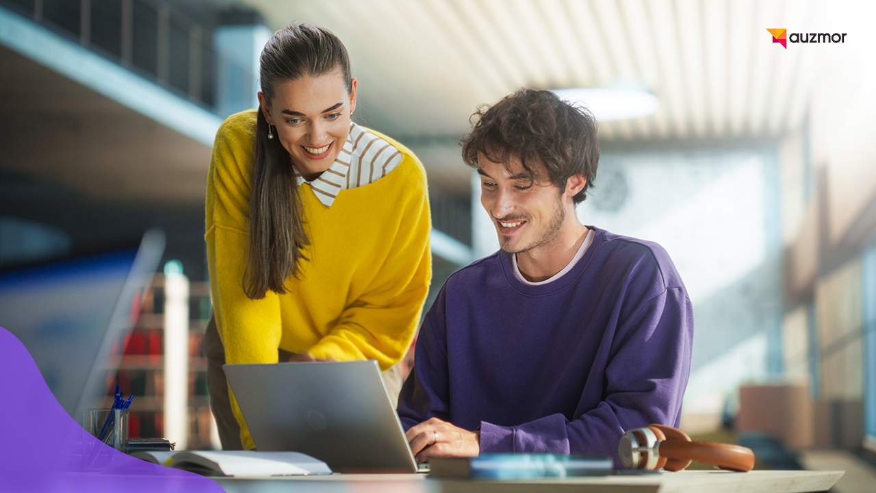 Two students smiling while working together on a laptop
