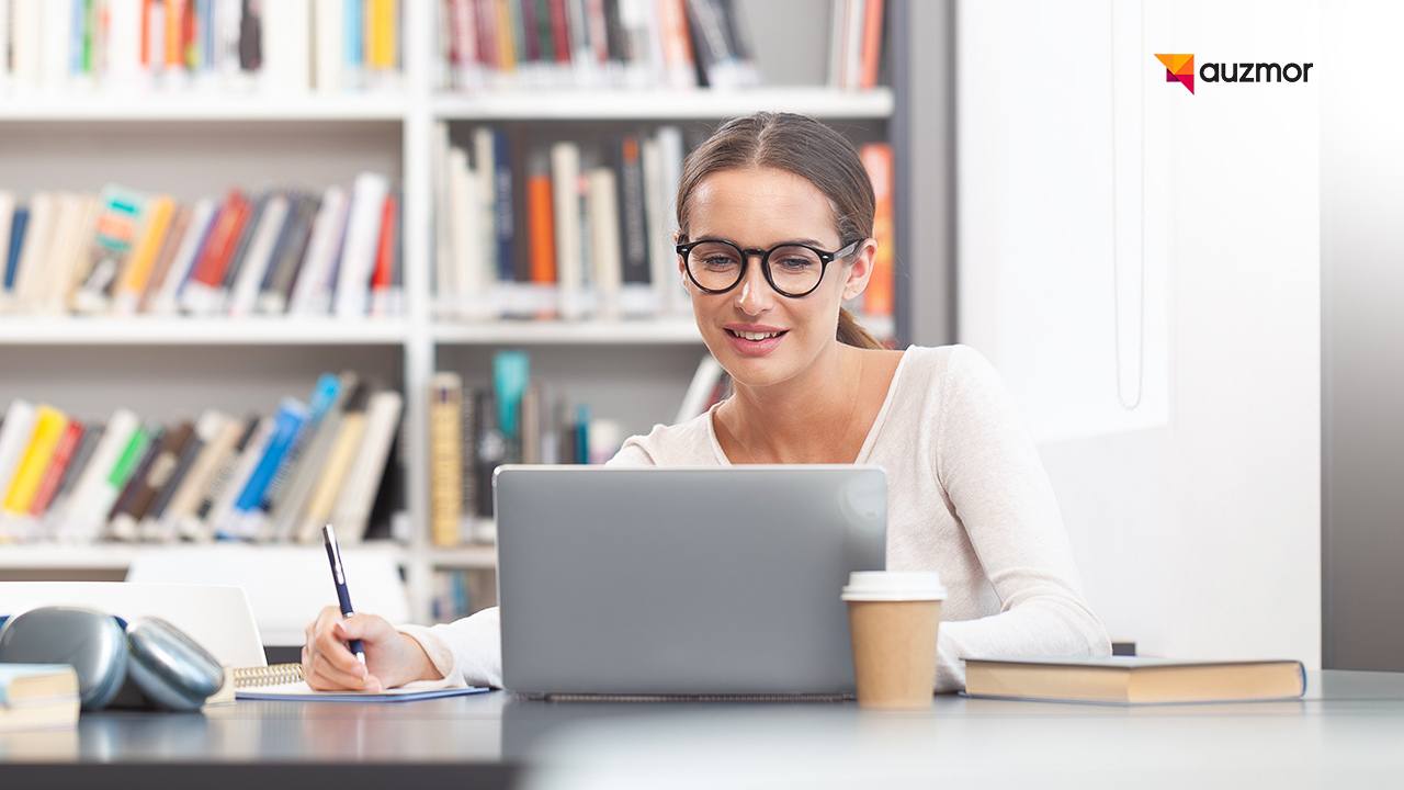 Educator taking notes at a laptop in front of a bookshelf
