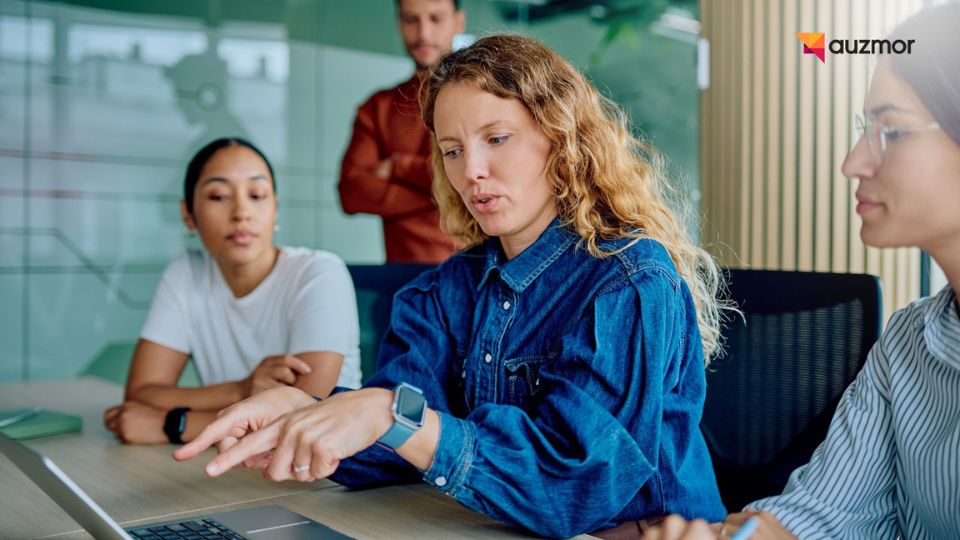 Colleague pointing at a laptop while two coworkers watch during a team discussion