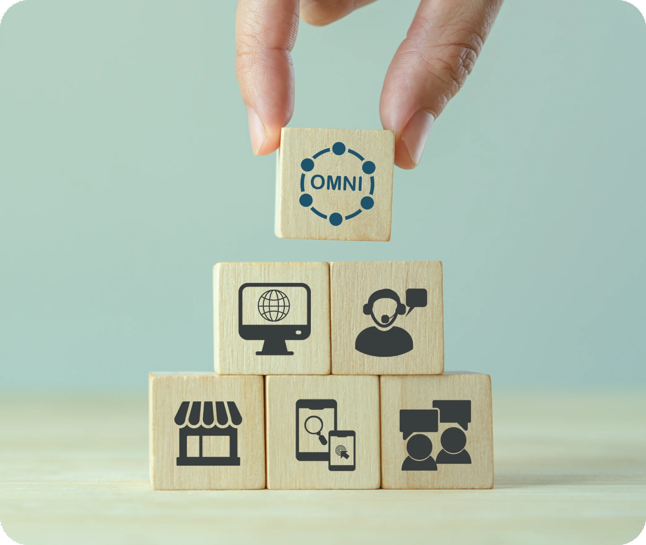 Hand stacking wooden blocks with channel icons topped by an omnichannel block