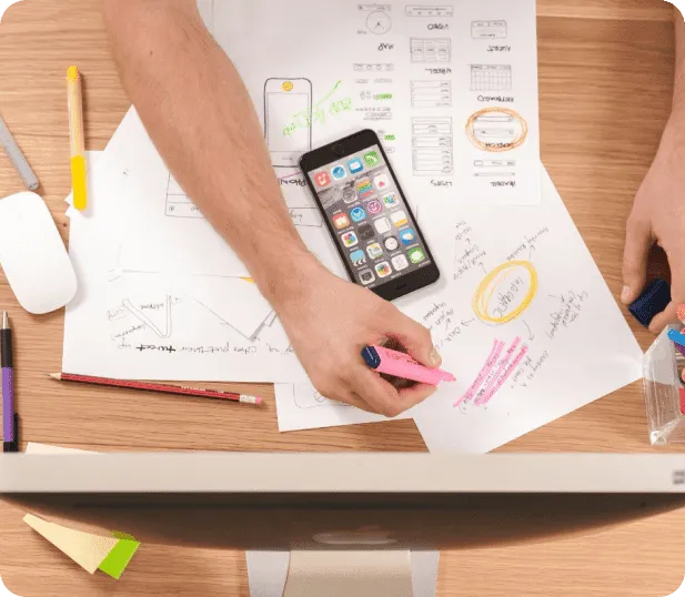 Hands sketching app wireframes on paper beside a smartphone