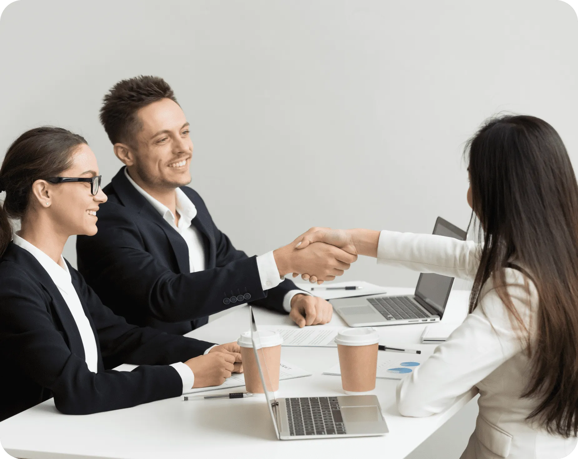 Two professionals shaking hands across a desk during a hiring interview