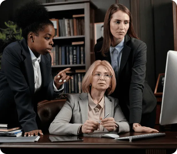 Three women in business attire reviewing training work together at a desk