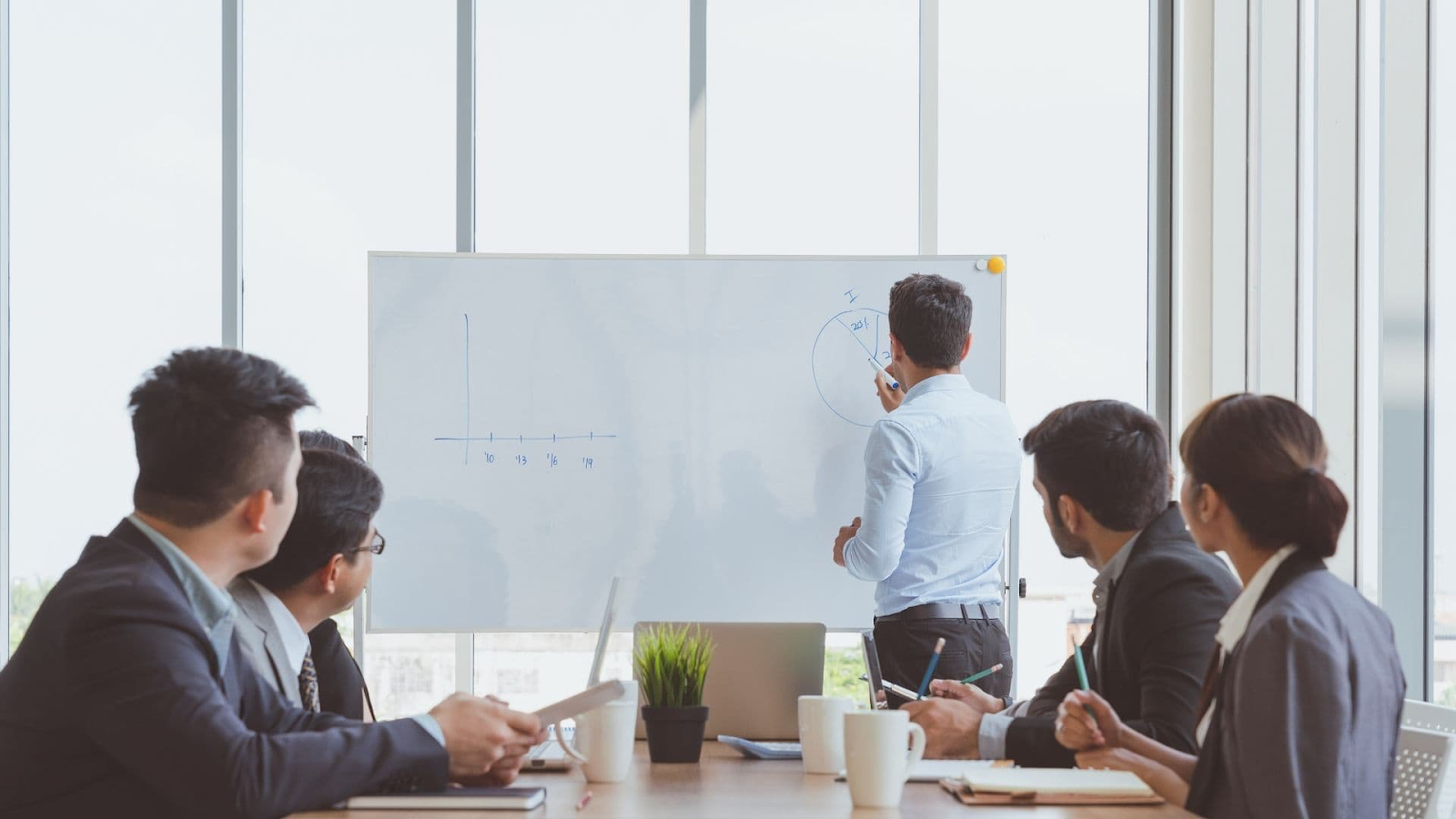 Trainer writing on a whiteboard while employees take notes in a meeting room